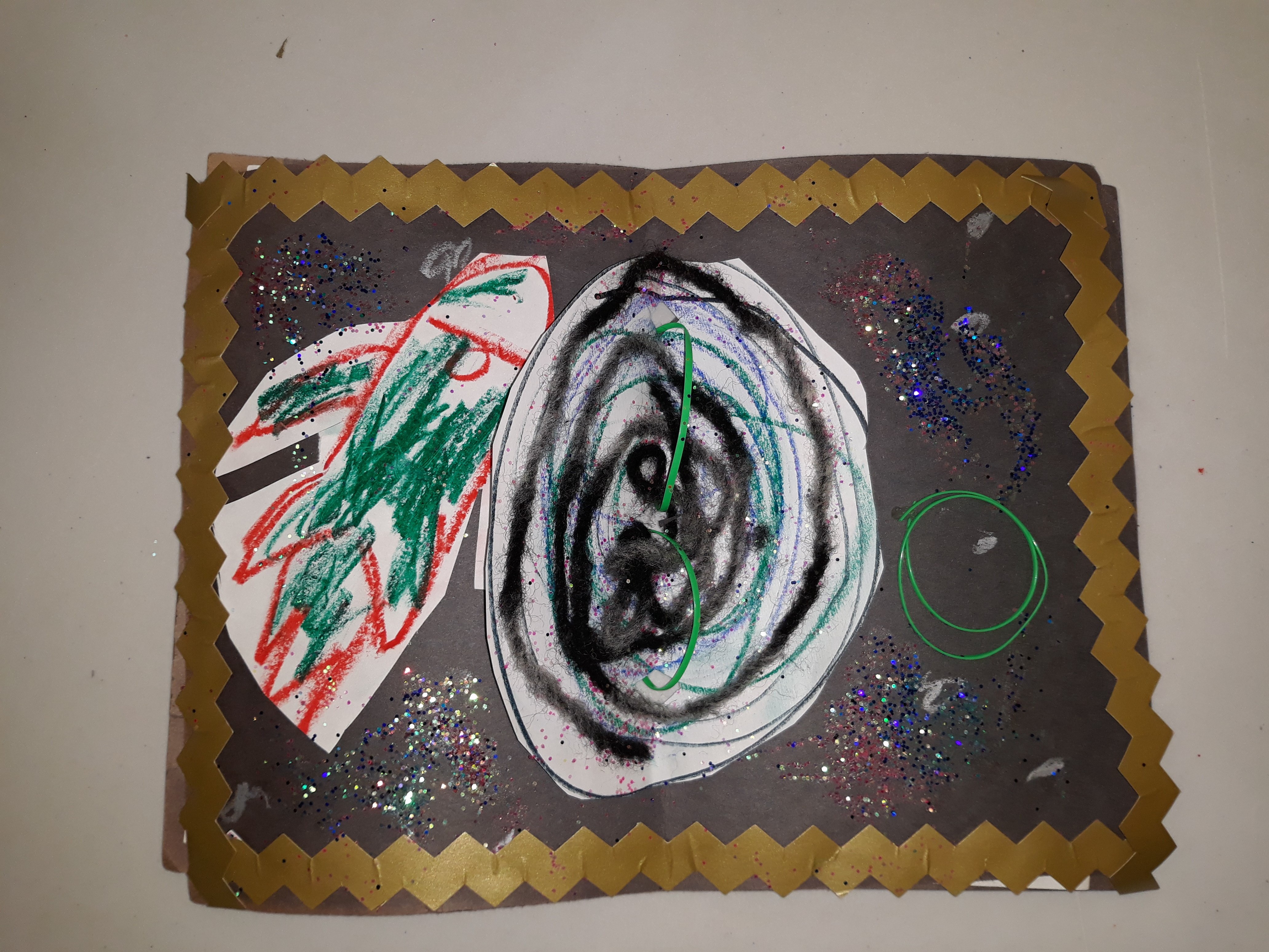 A swirling black hole takes center stage in this collage, made of yarn, gold trim, glitter, and other materials. 